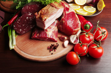 Meat products surrounded by vegetables on the kitchen board