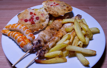 Grilled shrimp skewers. Scallops shell and surimi stick with fries. Wooden table