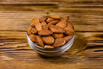 Glass bowl with the peeled almond nuts on wooden table