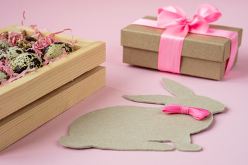 Obraz na płótnie Canvas Easter eggs in a wooden box on a pink background. Easter Bunny with a pink bow. Easter gift with pink ribbon. Empty for a greeting card. pink background is creative. Copy space