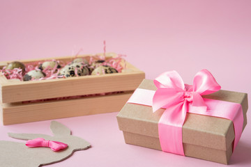 Easter eggs in a wooden box on a pink background. Easter Bunny with a pink bow. Easter gift with pink ribbon. Empty for a greeting card. pink background is creative. Copy space