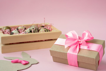 Easter eggs in a wooden box on a pink background. Easter Bunny with a pink bow. Easter gift with pink ribbon. Empty for a greeting card. pink background is creative. Copy space