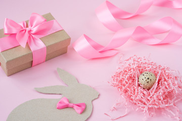Easter eggs in a wooden box on a pink background. Easter Bunny with a pink bow. Easter gift with pink ribbon. Empty for a greeting card. pink background is creative. Copy space
