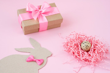 Easter eggs in a wooden box and nests. Easter Bunny with a pink bow. Easter gift with pink ribbon. Empty for a greeting card. pink background is creative.