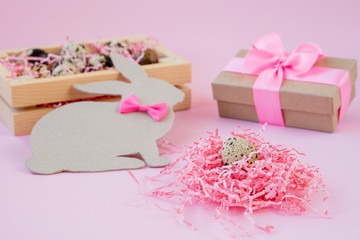 Easter eggs in a wooden box and nests. Easter Bunny with a pink bow. Easter gift with pink ribbon. Empty for a greeting card. pink background is creative.