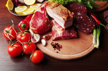 Meat products surrounded by vegetables on the kitchen board