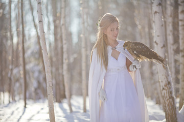 A beautiful girl in a white coat walks in the forest. The huntress with a bird in her hands.