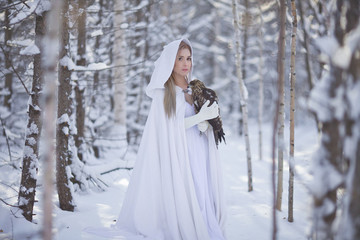 A beautiful girl in a white coat walks in the forest. The huntress with a bird in her hands.