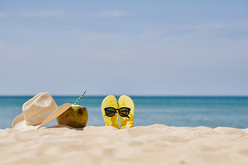 Yellow flip-flops, straw hat and sunglasses with cold delicious cocktail on sandy beach