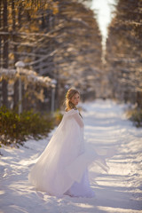 Fototapeta na wymiar Beautiful girl in a white dress walks in the winter forest. Bride on a background of a winter landscape