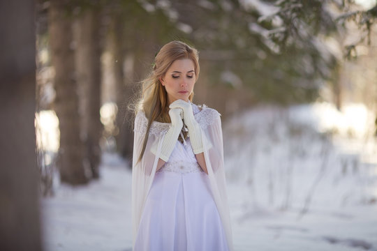 Beautiful girl in a white dress walks in the winter forest. Bride on a background of a winter landscape