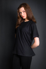 Beautiful, young girl with long hair, in black clothes, posing in studio on a gray background. A model with clean skin.