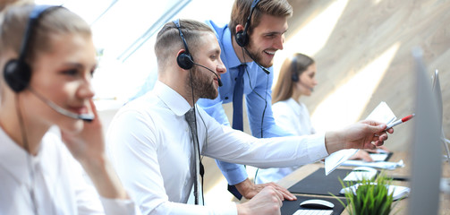 Phone operator working at call centre office helping his colleague.