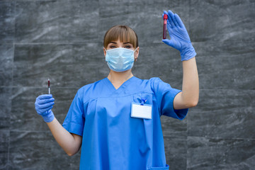 Young nurse with medical face mask is pointing at blood probe in laboratory. Medical concept.