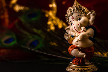 blurred red golden background with peacock feathers and ganesha statue in the foreground. religion...