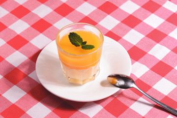 Mango Panna cotta with mango jelly and mint served in a glass ober red plaid tablecloth.