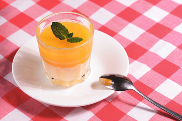 Mango Panna cotta with mango jelly and mint served in a glass ober red plaid tablecloth.