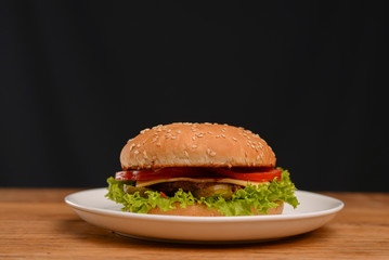 Classic burger served on white plate over black background. Meat hamburger flat lay. Junk food, fast food concept.