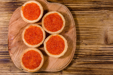 Tartlets with red caviar on a wooden cutting board. Festive food. Top view