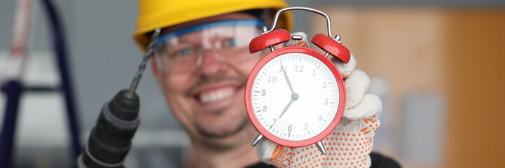 Focus on retro clock held by working man. Builder wearing helmet and glasses with protective lens....