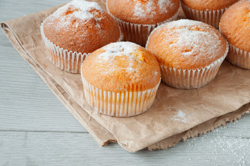 Fresh homemade delicious muffins are removed from the oven and refrigerated on a piece of paper on the kitchen table. Sprinkle muffins with sugar. Sweet dessert.