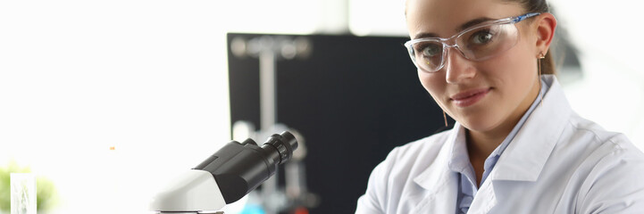 Portrait of attractive young female chemist posing in laboratory office. Microscope and medical...