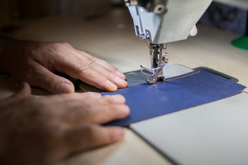 A man sews from leather on a sewing machine. Hands and sewing. Production of leather goods using a sewing machine