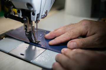 A man sews from leather on a sewing machine. Hands and sewing. Production of leather goods using a sewing machine