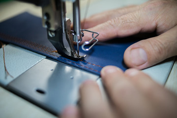 A man sews from leather on a sewing machine. Hands and sewing. Production of leather goods using a sewing machine