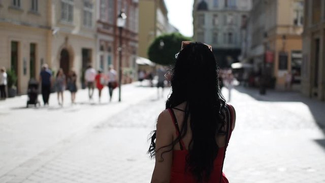 Young brunette woman is walking through the street, looking around and enjoying free time in historical part of Bratislava city in SLOW MOTION HD VIDEO. Half speed, rear view.