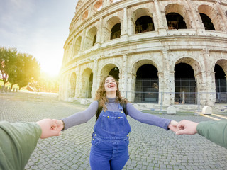 Young happy couple of tourists playing near at the Colosseum. Boy holding girl with his hands....