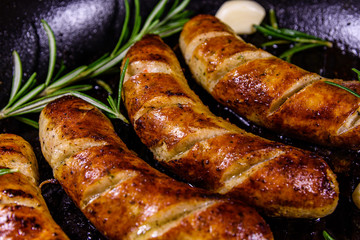 Roasted sausages with rosemary twigs and garlic in a cast iron grill pan