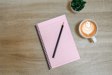 top view of notebook next to a pencil and cup of coffee on wooden table with copy space.