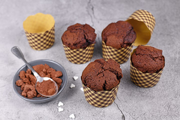 Homemade chocolate muffins in paper case with cup and spoon with cocoa powder on gray stone background
