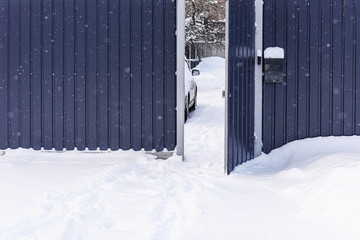 Footprints in the snow. Snow drifts. Winter, fence, snow on frosty day. Open gate in the fence on snowy day. Fence in the snow.