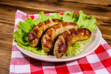 Plate with roasted sausages and lettuce leaves on a wooden table