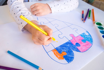 A child is drawing colorful heart with jigsaw puzzle on white background as a symbol of autism,...