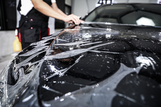 Close up of paint protection film installation on front bumper of modern luxury car. PPF is polyurethane film applied to car surface to protect the paint from stone chips, bug splatter, and abrasion