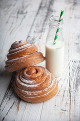 fresh homemade cinnamon rolls on a wooden cutting desk and milk in glass bottle