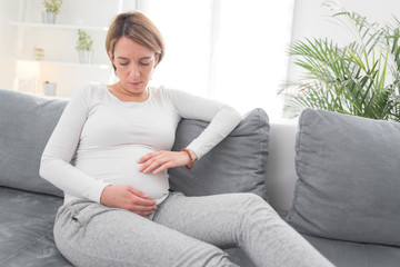 Pregnant tired exhausted woman with stomach issues at home on a couch, being sick.