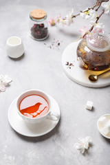 Spring tea party, tea time. Black tea in a cup with a reflection of bird and a teapot with flowering branches. Poster, greeting card, menu