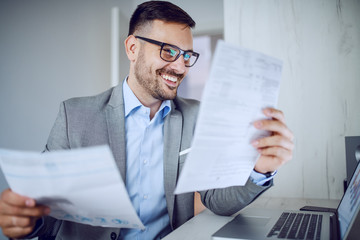 Hardworking sophisticated caucasian businessman in suit and with eyeglasses looking at documents...