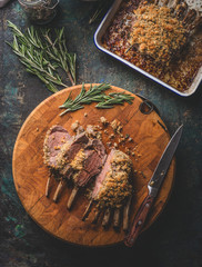 Tasty medium rare roasted lamb ribs with crust on wooden cutting board with rosemary and knife. Top...