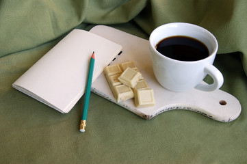 White cup with fresh coffee with a white bar of chocolate with whole hazelnuts.