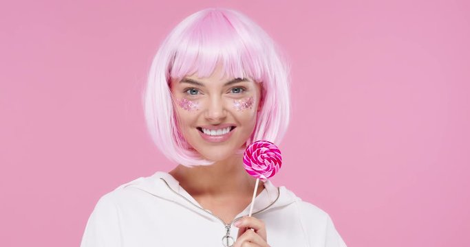 Beauty model woman with trendy pink hair style and beautiful glitter makeup holding colorful sweet lollipop candy