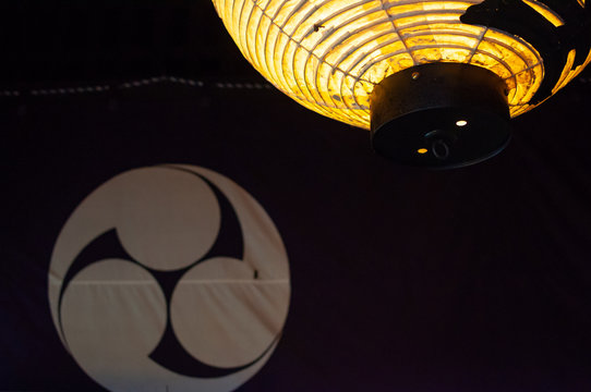 Japanese paper lantern lit and a fabric screen with emblem on background
