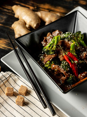 Asian style served restaurant dish with roasted meat and vegetables on black plate background.