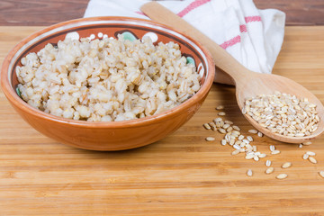 Pearl barley porridge in bowl, uncooked pearl barley close-up