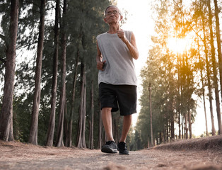 Asian senior man jogging in the park over sunset sky background. Healthy lifestyle and Healthcare concept.