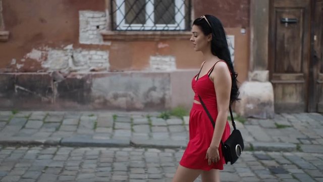 Young brunette woman is walking through the street, looking around and enjoying free time in historical part of Bratislava city in SLOW MOTION HD VIDEO. Half speed, side view.